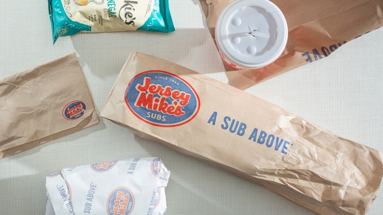 A Jersey Mike's sub and sides with a napkin, drink, and bag of Miss Vickie's chips