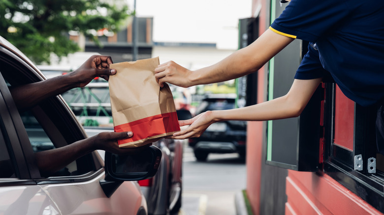 fast food worker handing customer a bag from drive thru window