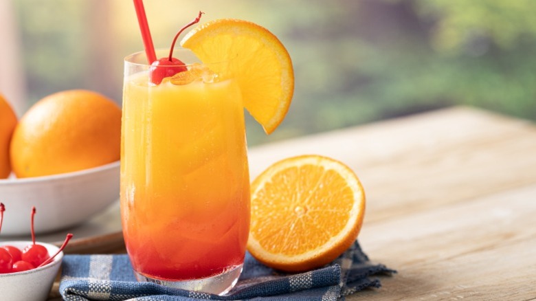 A tequila sunrise cocktail with cherry and orange garnishes on wooden table.