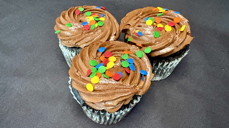 three chocolate cupcakes with rainbow sprinkles