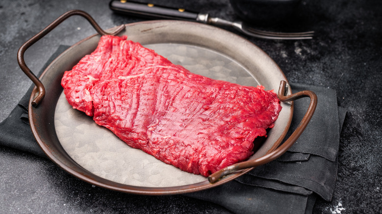 Uncooked flank steak on a metal platter next to a fork