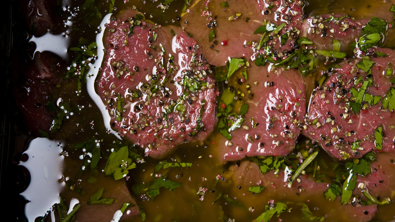 Pieces of cut beef steak in a marinade with fresh herbs and spices