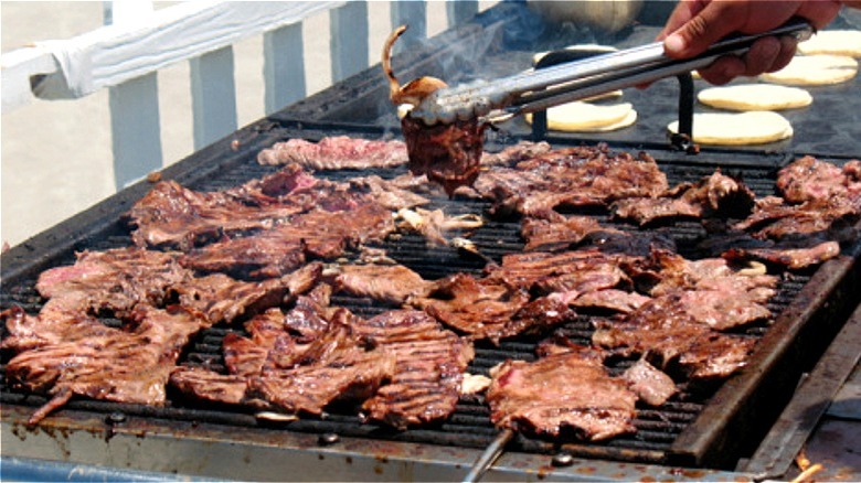 Skirt steak grilled on an open outdoor grill as a person flips one piece with tongs