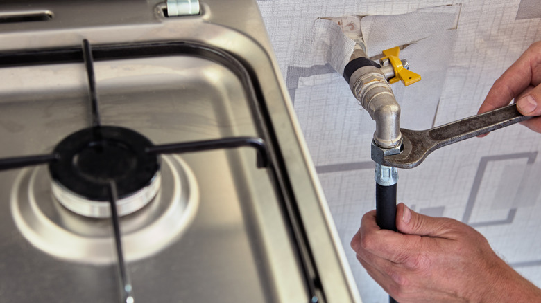 Hands screwing gas line into wall fixture next to gas stove