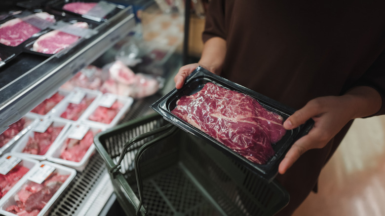 Customer picking up meat from the refrigerated section of a grocery store