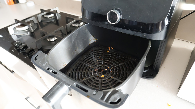 Black air fryer with drawer open on kitchen counter next to stove