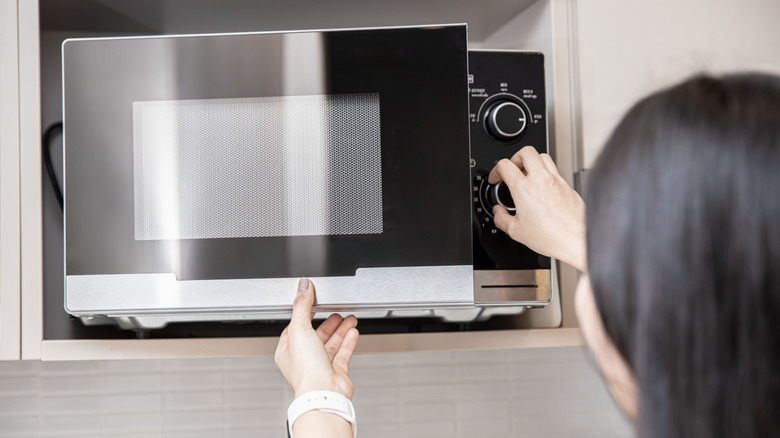 Black and silver microwave oven with person opening door and adjusting settings