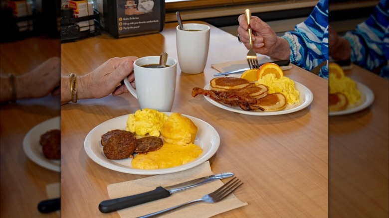 Two diners seated at restaurant table eating breakfast food.