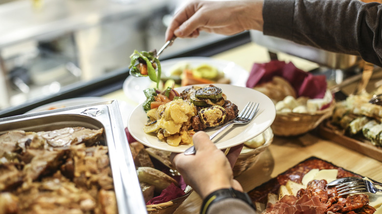 Person at buffet-style restaurant adding food to their plate.