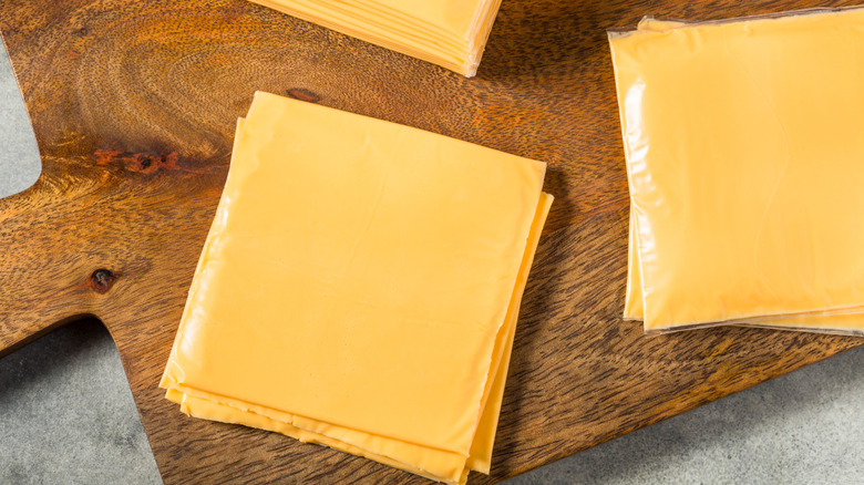Slices of American cheese in wrappers on cutting board