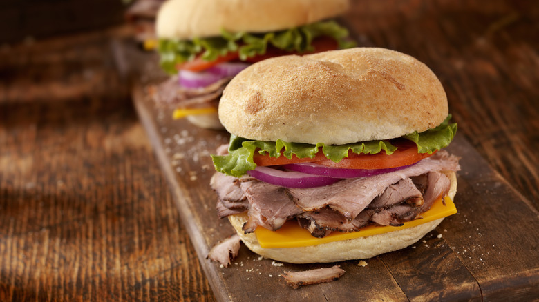 Roast beef sandwiches on cutting board with lettuce, tomatoes, and onions.