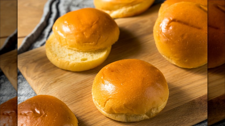 Several brioche bread rolls on a wood cutting board.