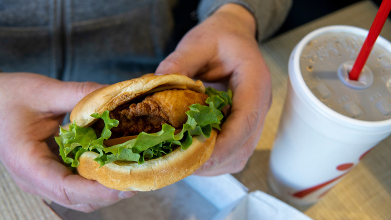 Hands holding a Deluxe chicken sandwich from Chick-fil-A with drink nearby