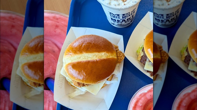 A Culver's chicken sandwich on tray at the restaurant surrounded by other food and drinks.