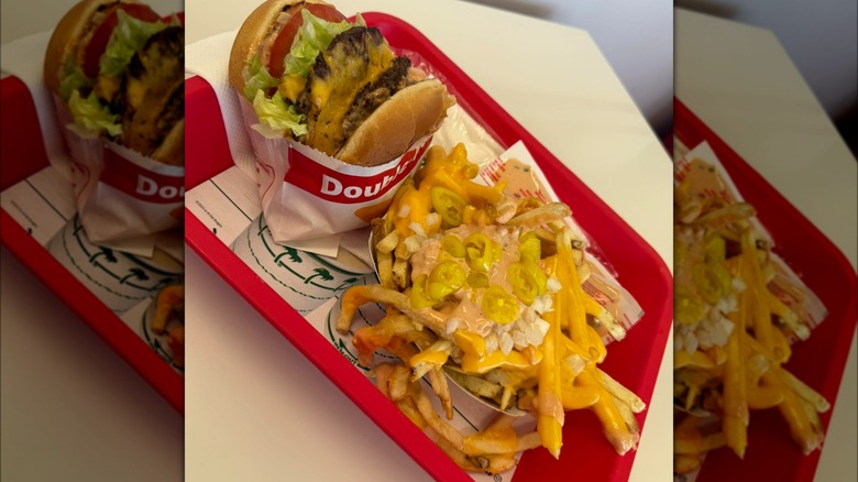 A mustard-grilled double burger and loaded french fries on tray inside In-N-Out.