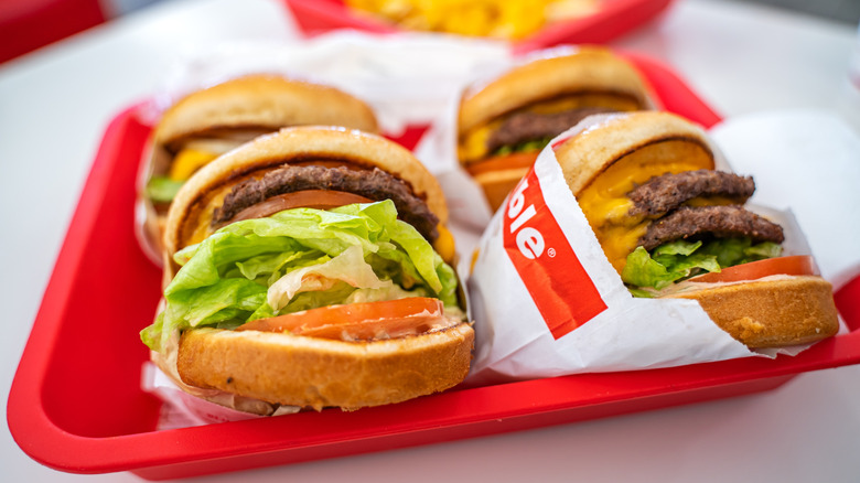 Four burgers from In-N-Out wrapped in paper and sitting on tray.