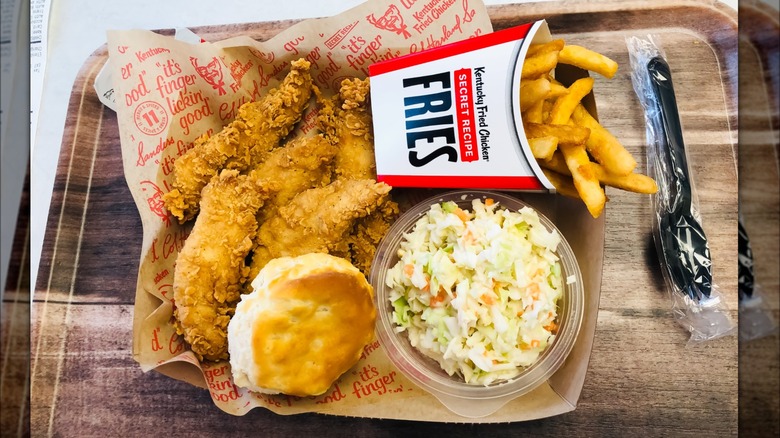 A tray with items from KFC: chicken tenders, fries, biscuit, and coleslaw.