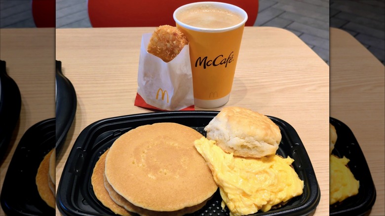 McDonald's breakfast tray with scrambled eggs, biscuit, and pancakes, plus hashbrown patty and coffee.