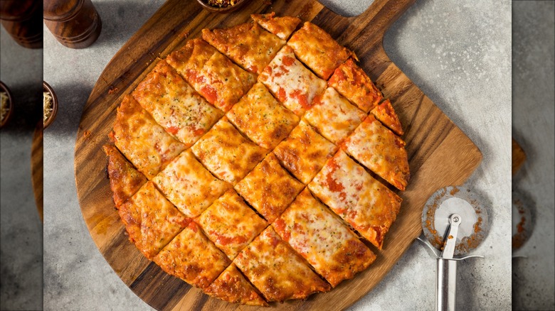 Thin crust, tavern-style pizza on cutting board next to pizza cutter.