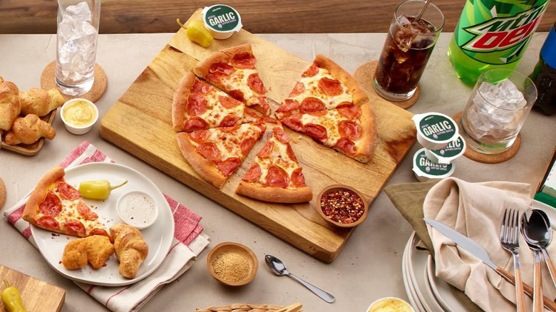 Papa John's pepperoni pizza with sauce and seasonings on cutting board.