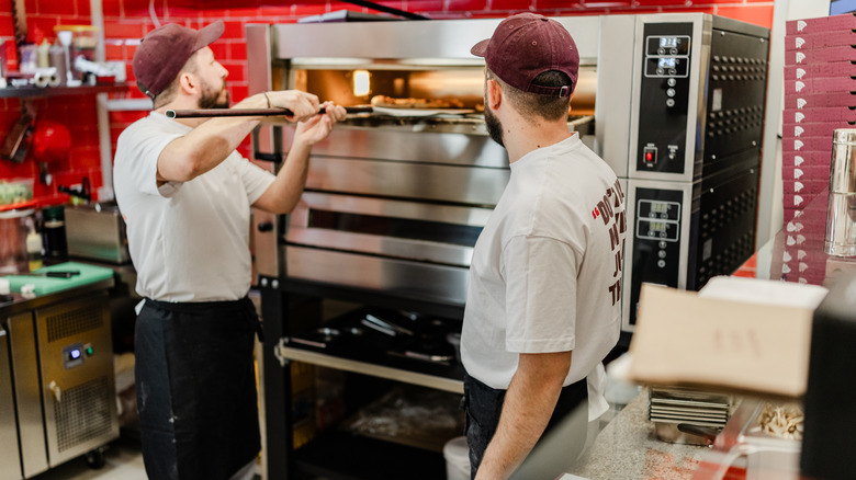 Two chefs removing pizza from oven.