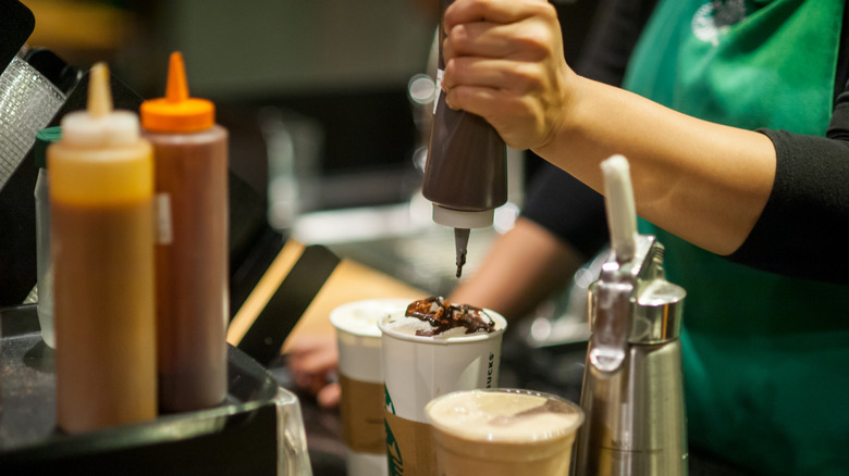 Starbucks barista adding chocolate syrup to coffee beverage.