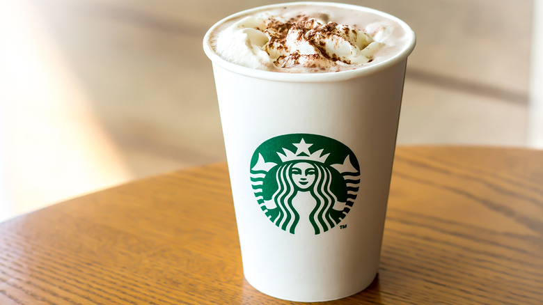 Tall-size Starbucks paper cup with whipped cream and cinnamon on top.