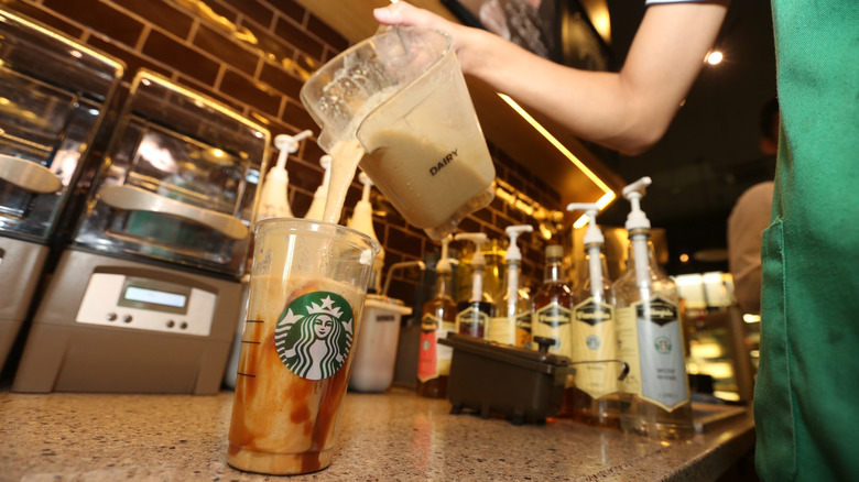 ﻿Barista at Starbucks pouring dairy concoction into a plastic cup.