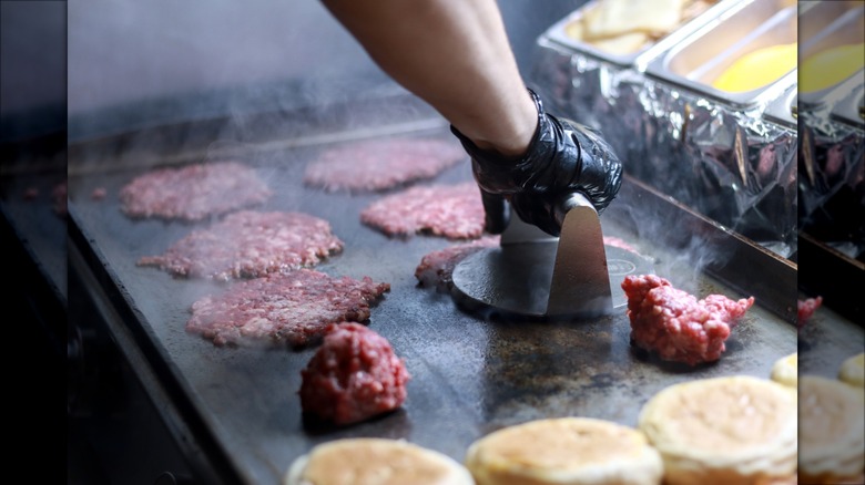 Person grilling several smash burgers in commercial kitchen.