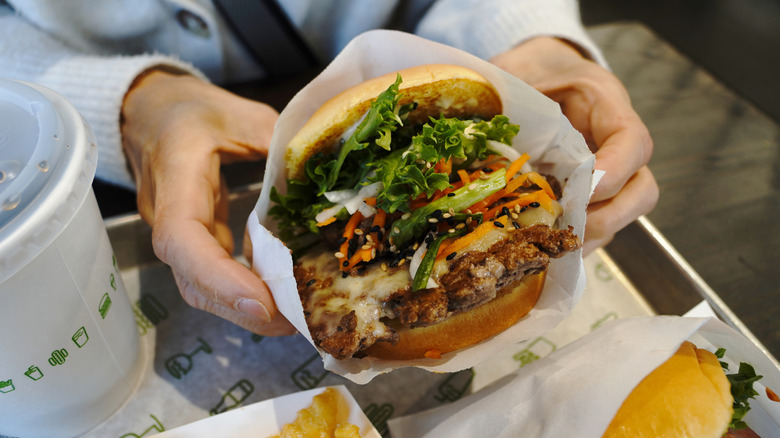 Person holding giant Shake Shack burger over tray with both hands.