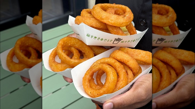 Person holding three cartons of Shake Shack onion rings.