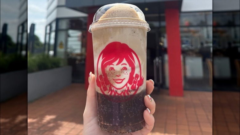 A person holding a Wendy's Frosty mixed with cola.