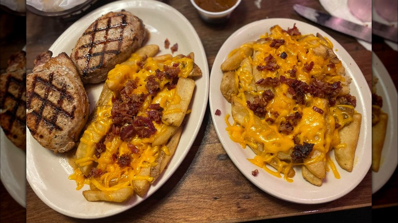 Plates on table at Texas Roadhouse, one with cheese fries & two chops and the other with cheese fries.