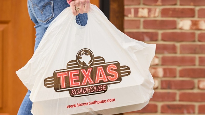Person carrying large to-go bag with the Texas Roadhouse logo on the front.