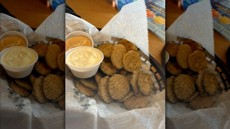 Texas Roadhouse fried pickles in a plastic basket with paper and cups of dipping sauces.