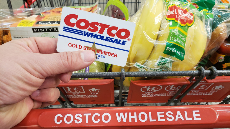 Hand holding Costco membership card over shopping cart with groceries