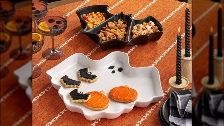 A Halloween table setting with themed serving trays, candles, and drinks.