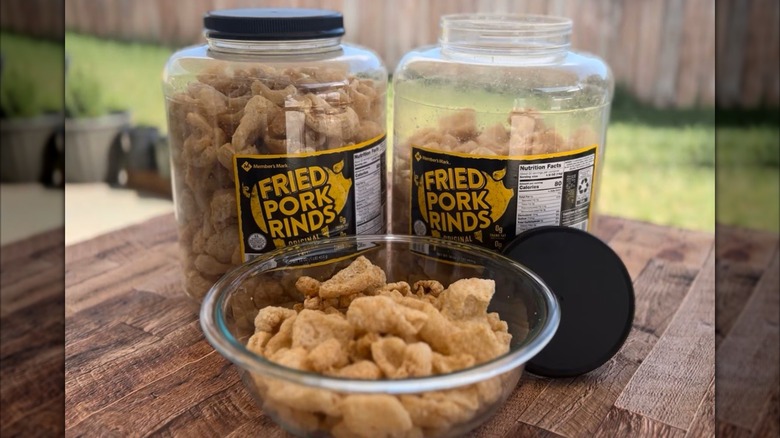 A bowl of fried pork rinds with two large tubs of the snacks in the background.