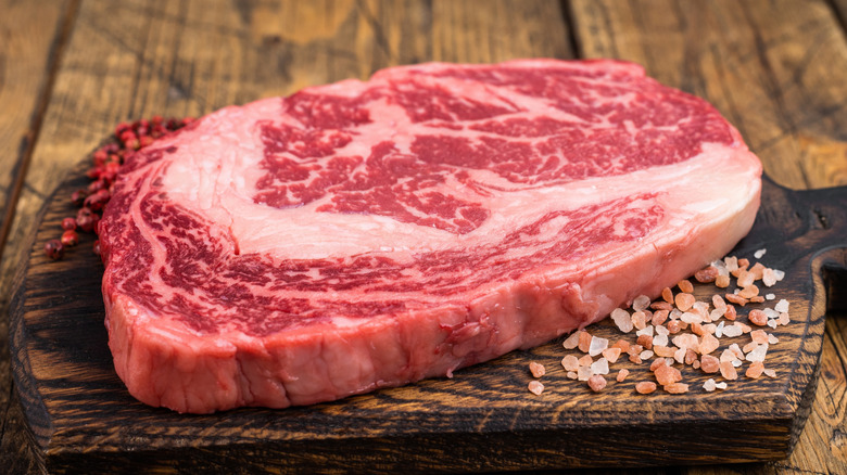 Raw ribeye steak with large cap and fat marbling on wooden cutting board.