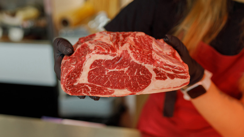 Butcher holding up marbled ribeye steak.