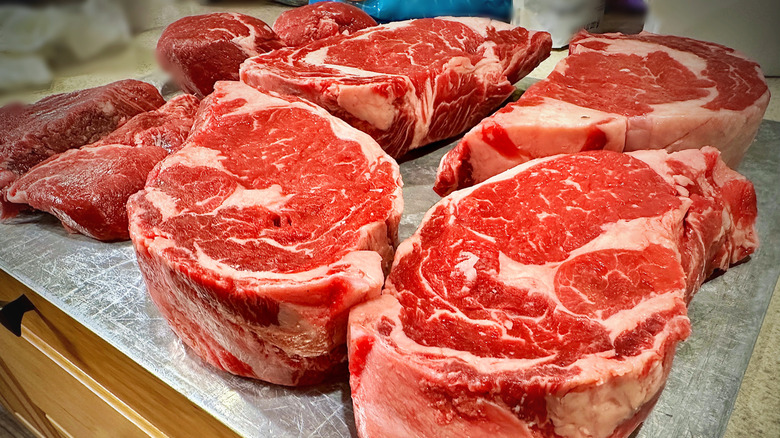 Raw, thick-cut ribeye steaks on metal surface.