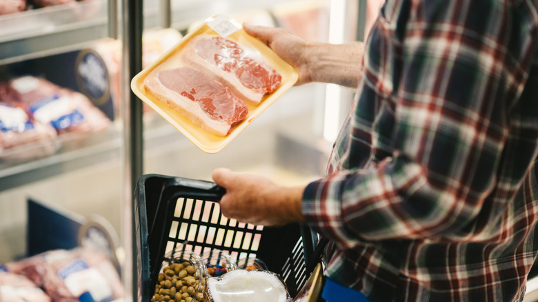 shopper looking at package of steak in grocery store
