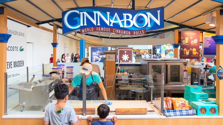 Two children watching a Cinnabon employee make cinnamon rolls.