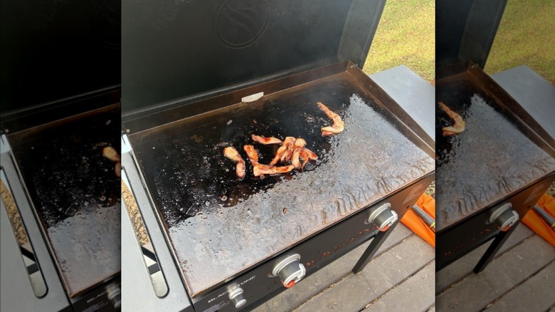 Bacon cooking on Blackstone grill outside.
