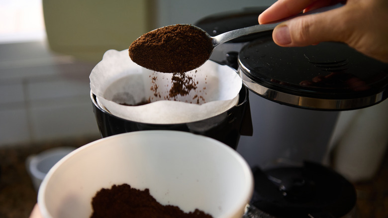 Hand spooning coffee into drip coffeemaker filter.