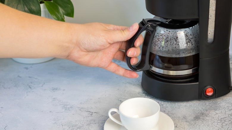 Hand reaching out for drip coffeemaker carafe.