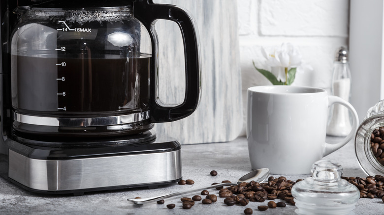 Drip coffeemaker with cup and whole coffee beans.