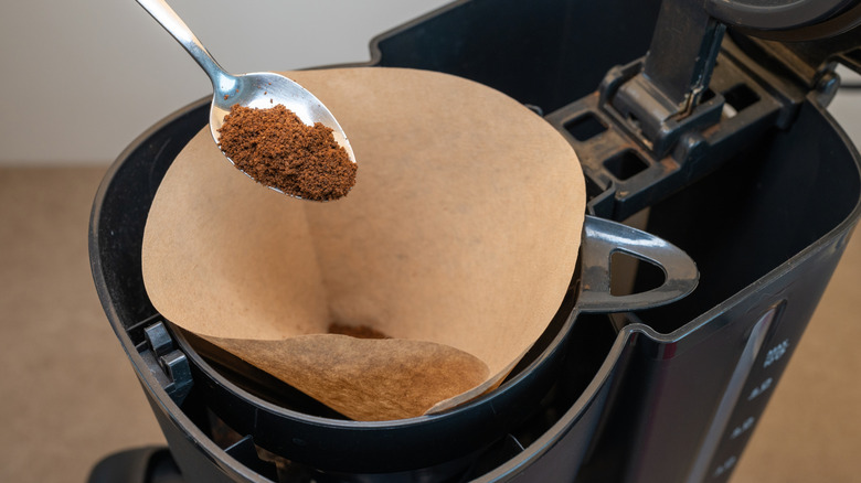 Coffee being spooned into a paper filter in a drip machine