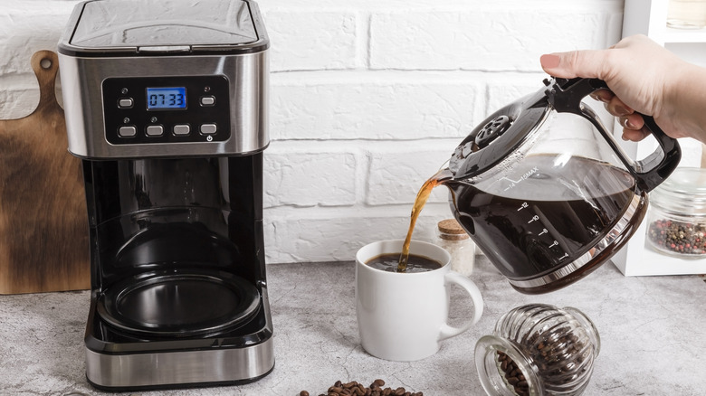 Coffee being poured from a carafe into a cup next to its drip coffee maker