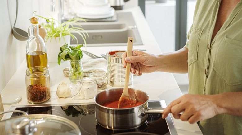 Closeup of person stirring simmering tomato sauce on an induction stovetop